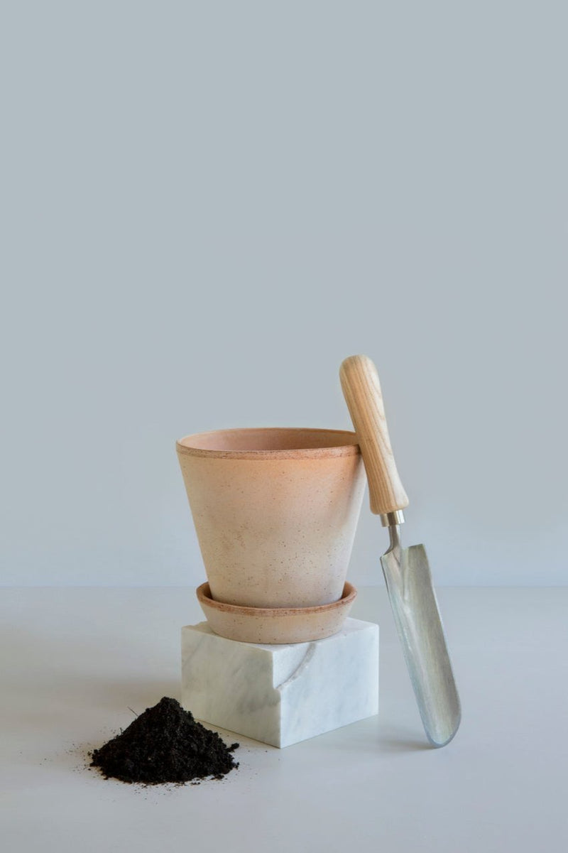 Bergs Potter Julie Rosa pot standing on a white display brick with a shovel and a pile of soil ready to plant.