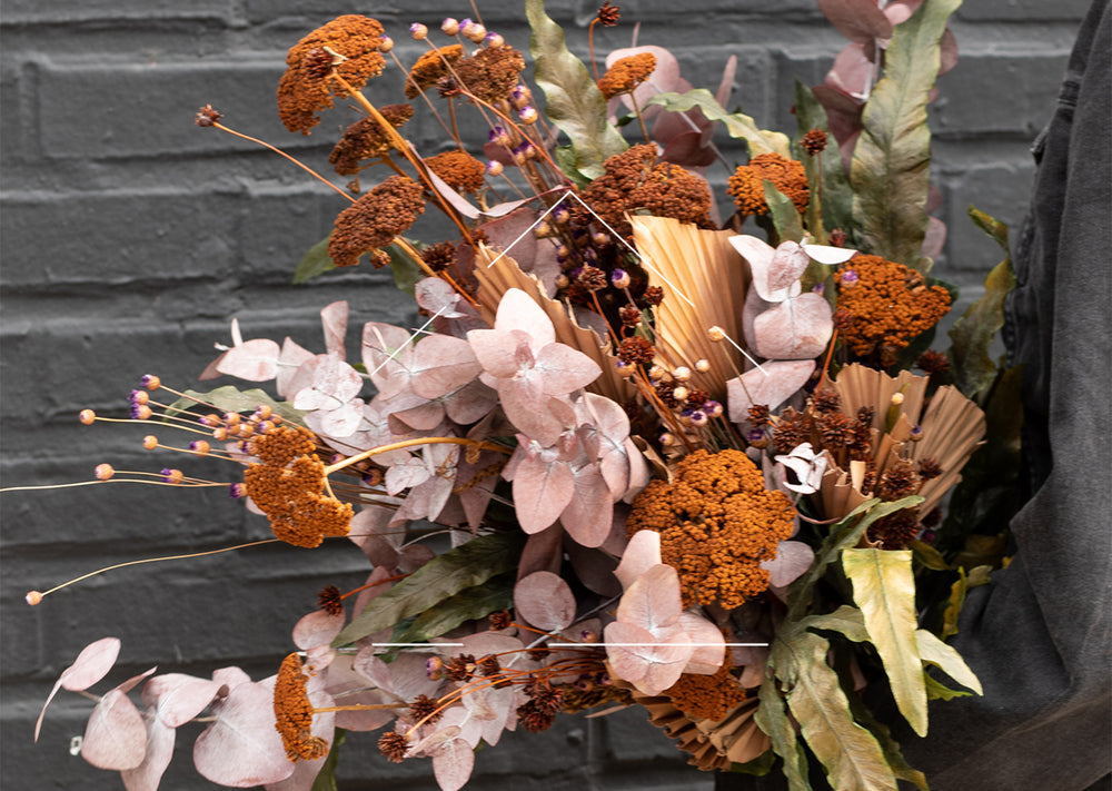 Dried floral arrangement in tones of brown, cream, green and rust against black wall. 