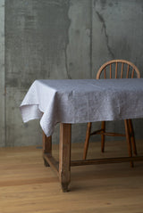 Grey and white striped tablecloth on a wood farm table on a wood floor and a concrete wall. 