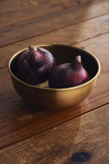 Extra Large brass bowl by Fog Linen Work holding two onions on top of a wood table.