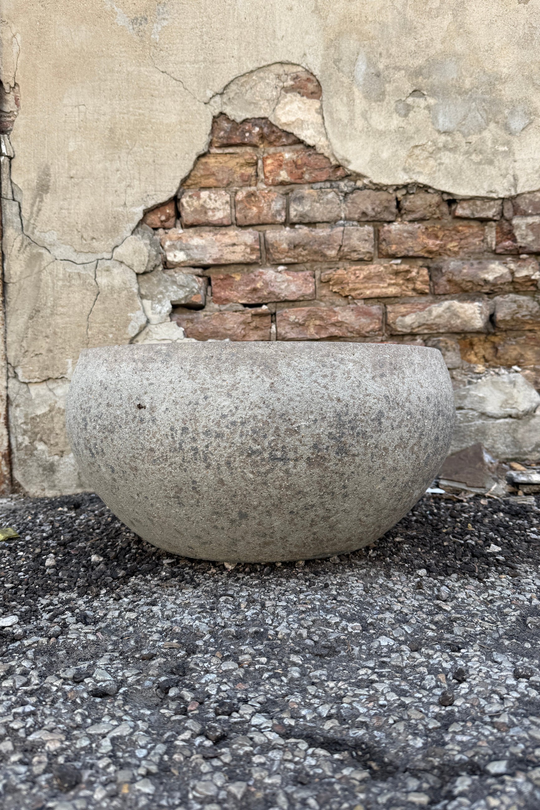 Low Ficonstone Greige Low Bowl Large on a stone pavement with a textured wall in the background ©Sprout Home