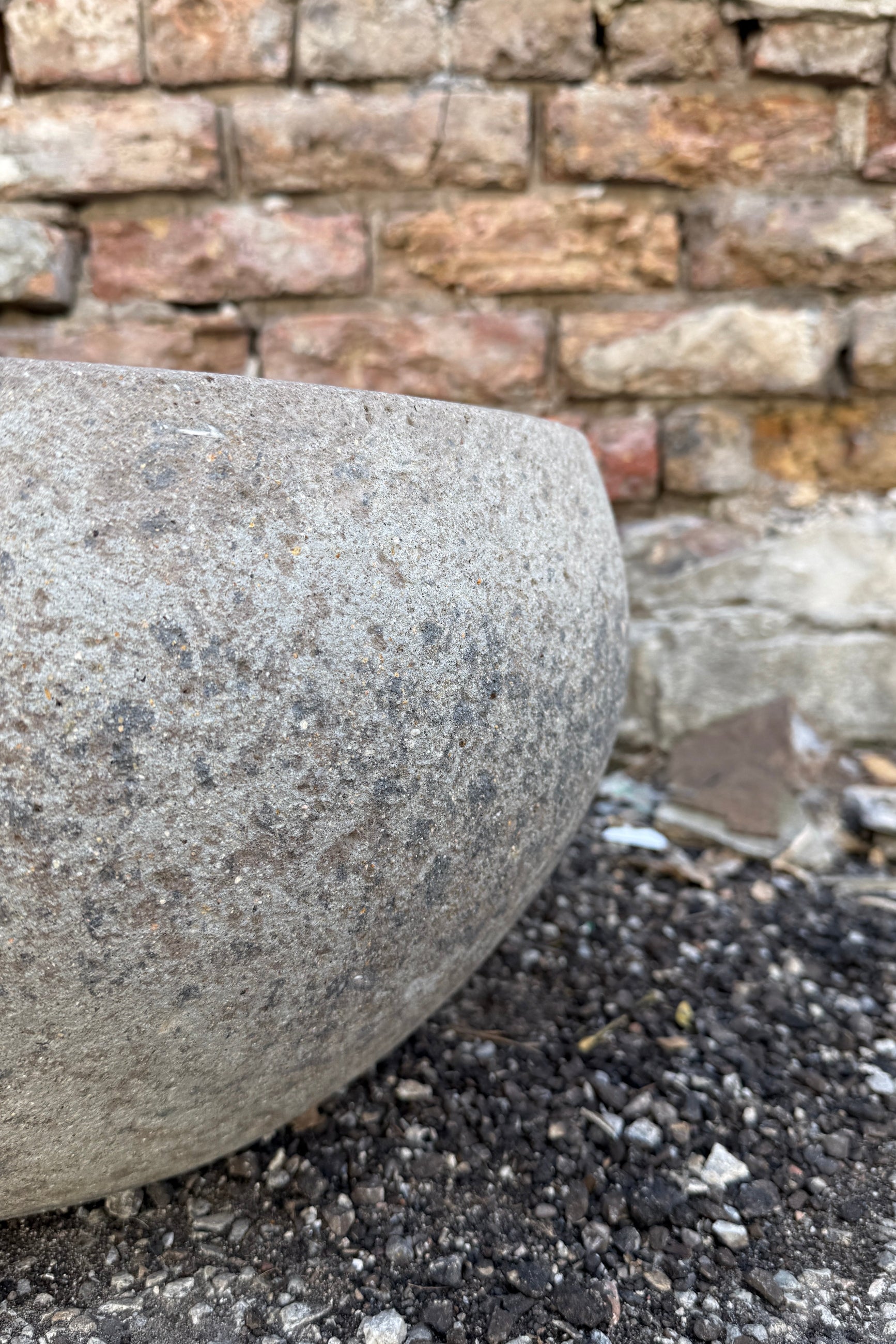 Close-up of a Low Ficonstone Greige Low Bowl Large on a gravel surface with a brick wall in the background ©Sprout Home