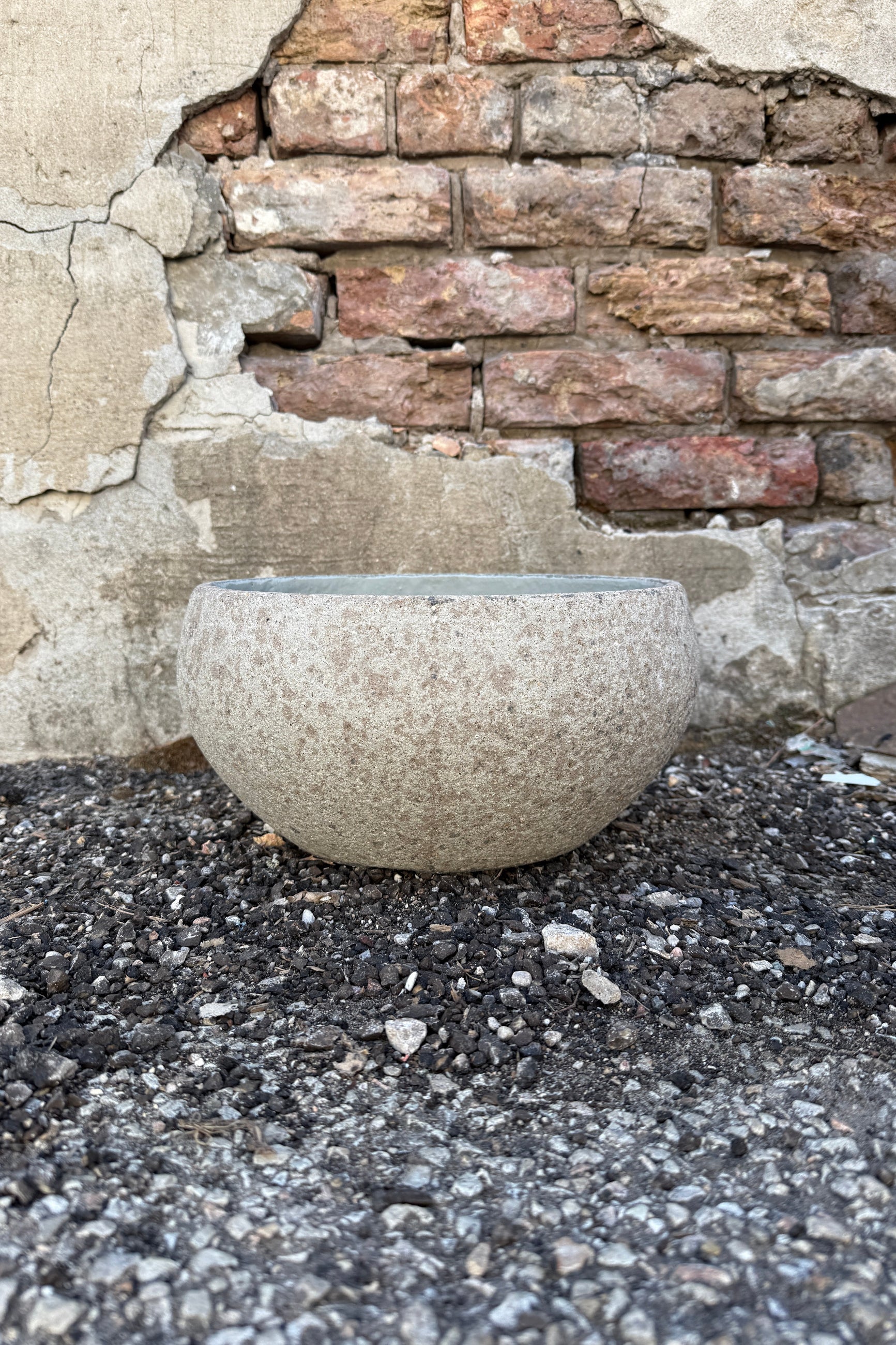 Low Ficonstone Greige Bowl Small on a gravel surface with a brick wall background ©Sprout Home