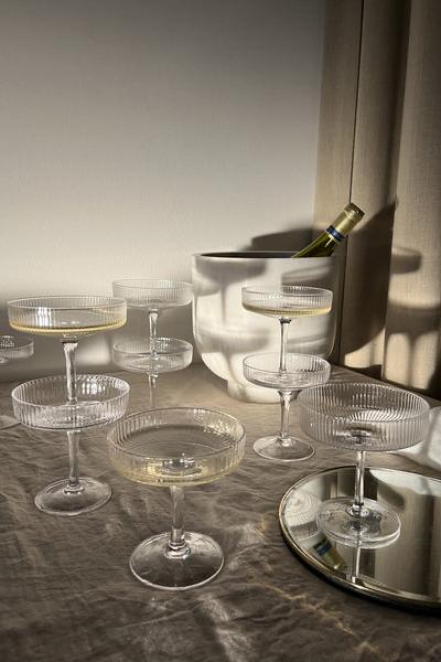 A handful of clear Ripple champagne glasses in a lifestyle shot with a bucket of champagne in the background and some of the glasses filled.