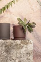 Rust colored Medium Sekki Pot by Ferm Living in a lifestyle shot against a pink wall. 