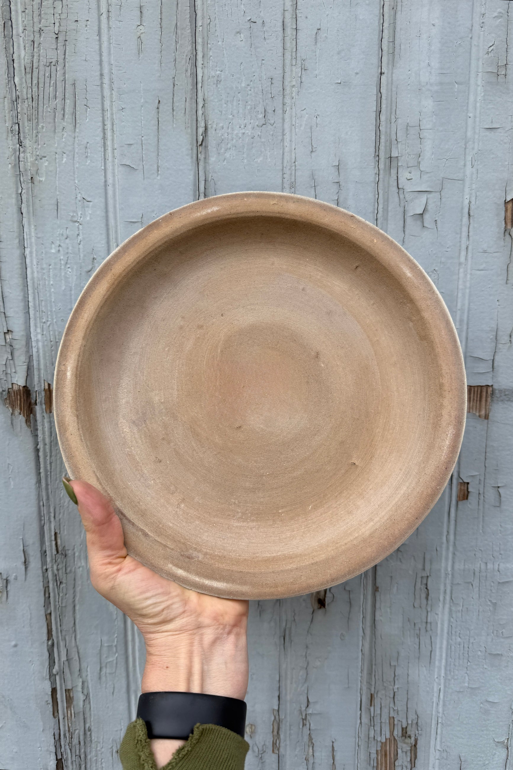 Hand holding a ceramic 11" saucer against a wooden background ©Sprout Home