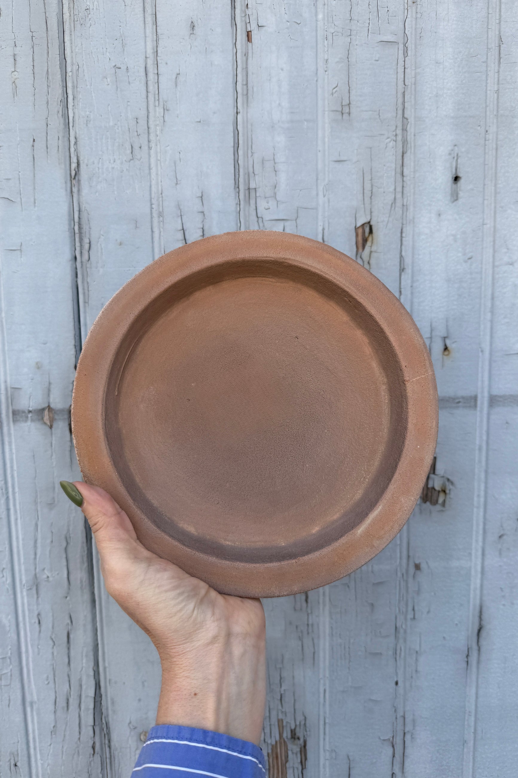 Hand holding a terracotta saucer against a wooden background ©Sprout Home