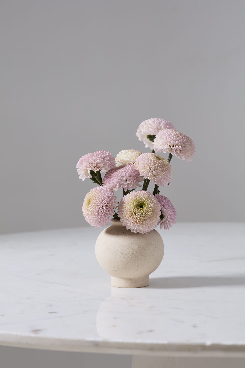 Small bouquet of pink and white flowers in a beige Stockton vase on a marble surface with a gray background ©Accent Decor