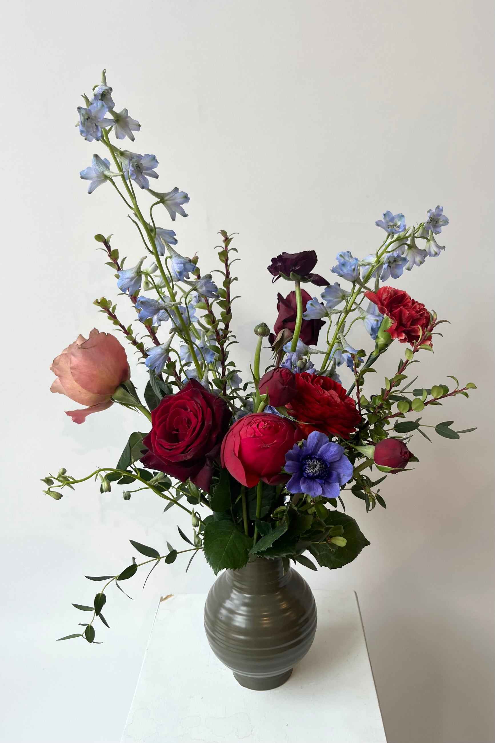 Sprout Home Storm arrangement with shades of purple and blue being held against a white wall in August  ©Sprout Home #size_$75