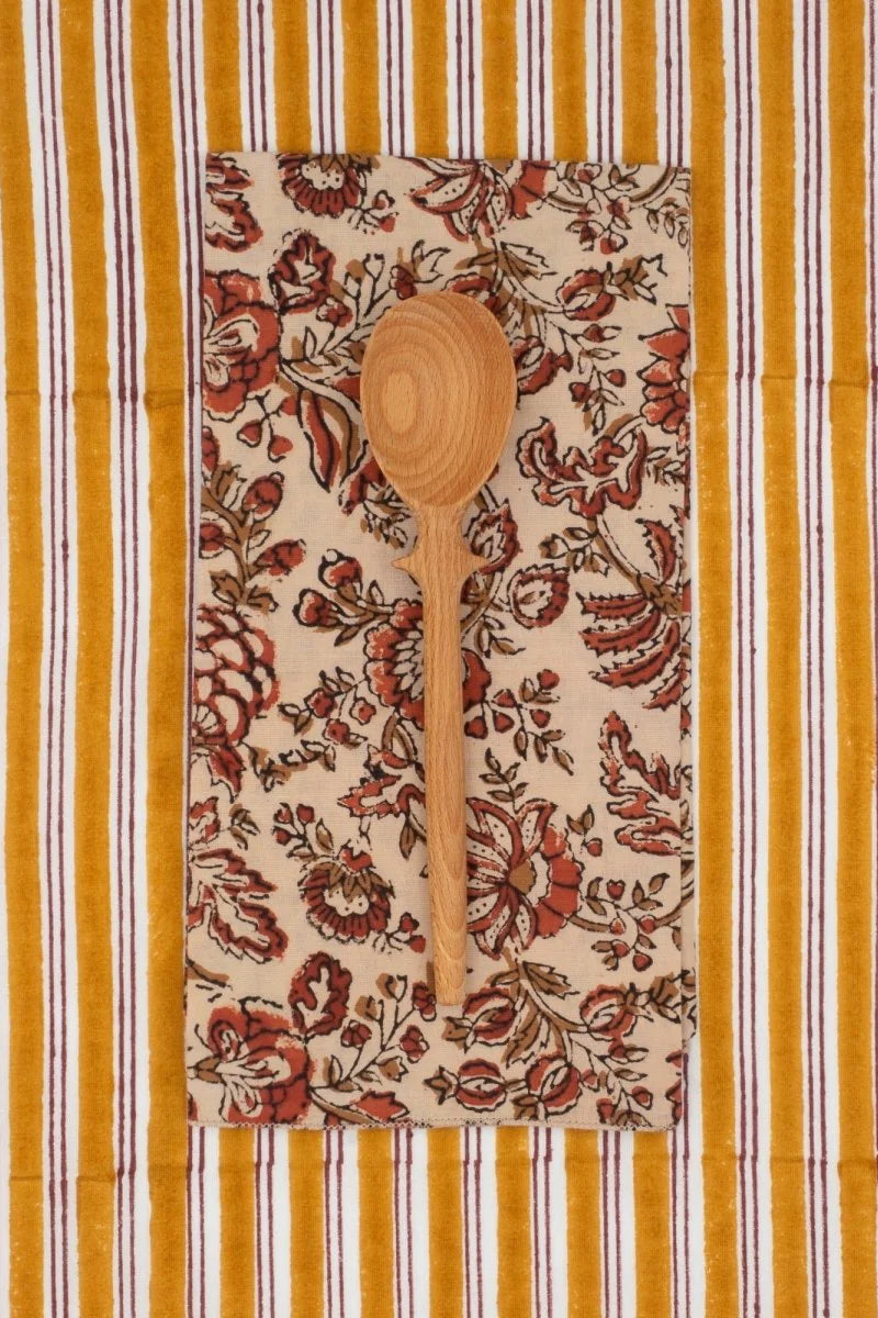 Cotton Napkins Melisse Ecureuil sitting on a striped cloth and a wooden spoon on top ©Suzette a Table