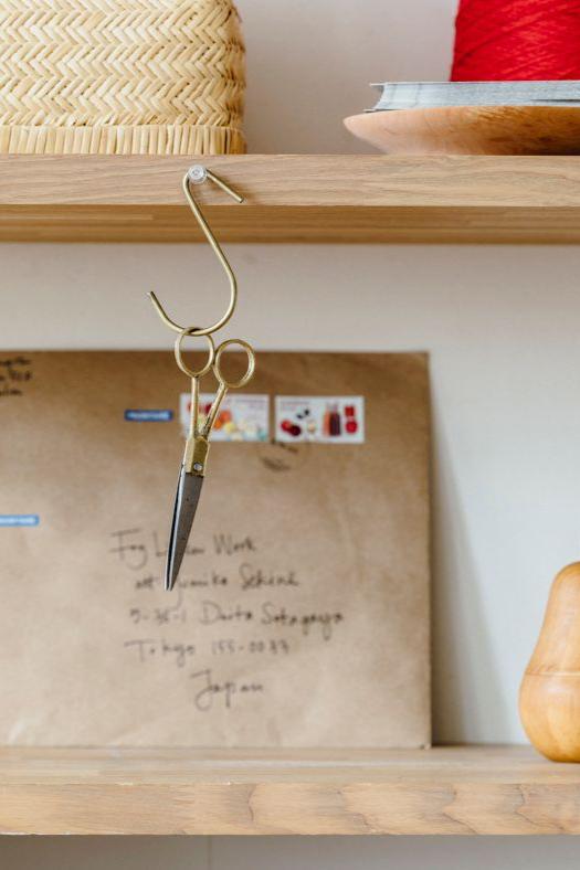 Small brass hook by Fog Linen Work hanging from a shelf holding a pair of scissors.