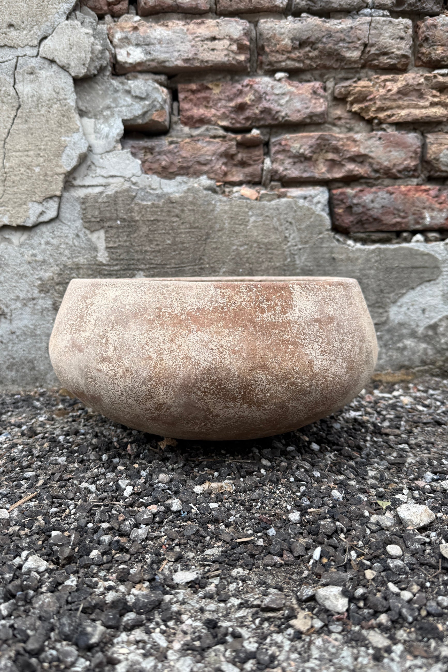 Sansui Tapered Vietnamese Rustic Bowl Medium on a gravel surface with a brick wall background ©Sprout Home