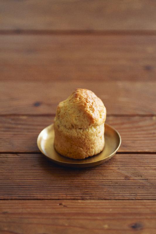 Small brass plate by Fog Linen Work with a muffin on top of it and the plate is sitting on a wood table. 