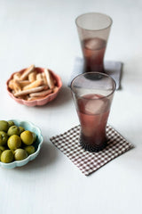 Joshu Linen Coaster by Fog Linen Work up front with a filled glass on top in a lifestyle shoot with bowls of snacks. 