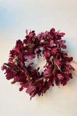 The Sprout Home Quercus Ruby Wreath being held against a white wall. 