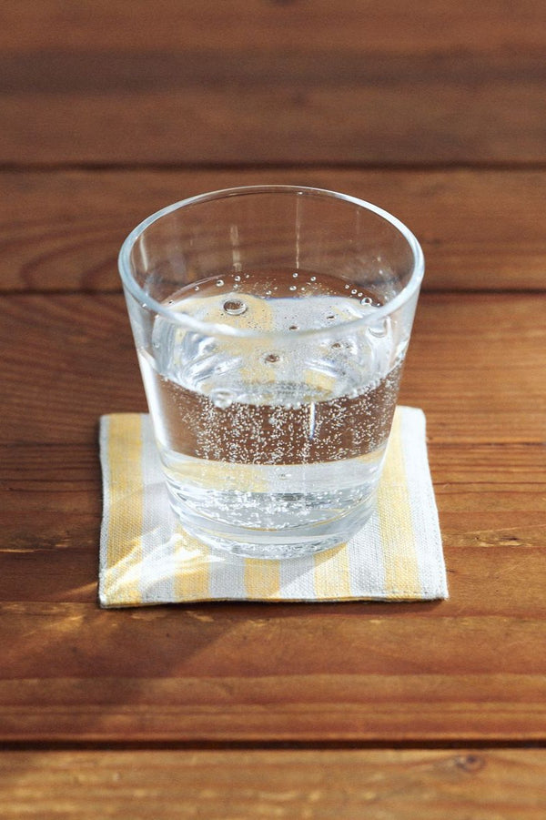 Henry  Linen coaster by Fog Linen Work sitting on a wood table and a glass with water on top