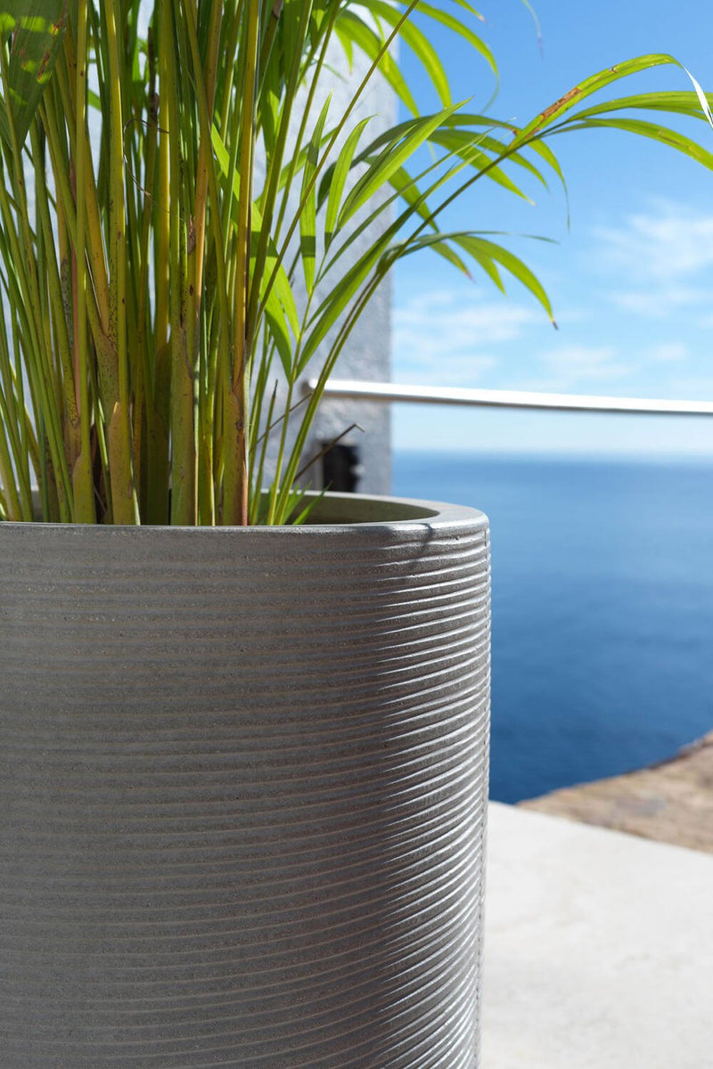 Pottery Pots Cody High Dark Grey Horizontal Ridged Pot  up close showing the ridges, a palm inside and on a deck with water in the distance.