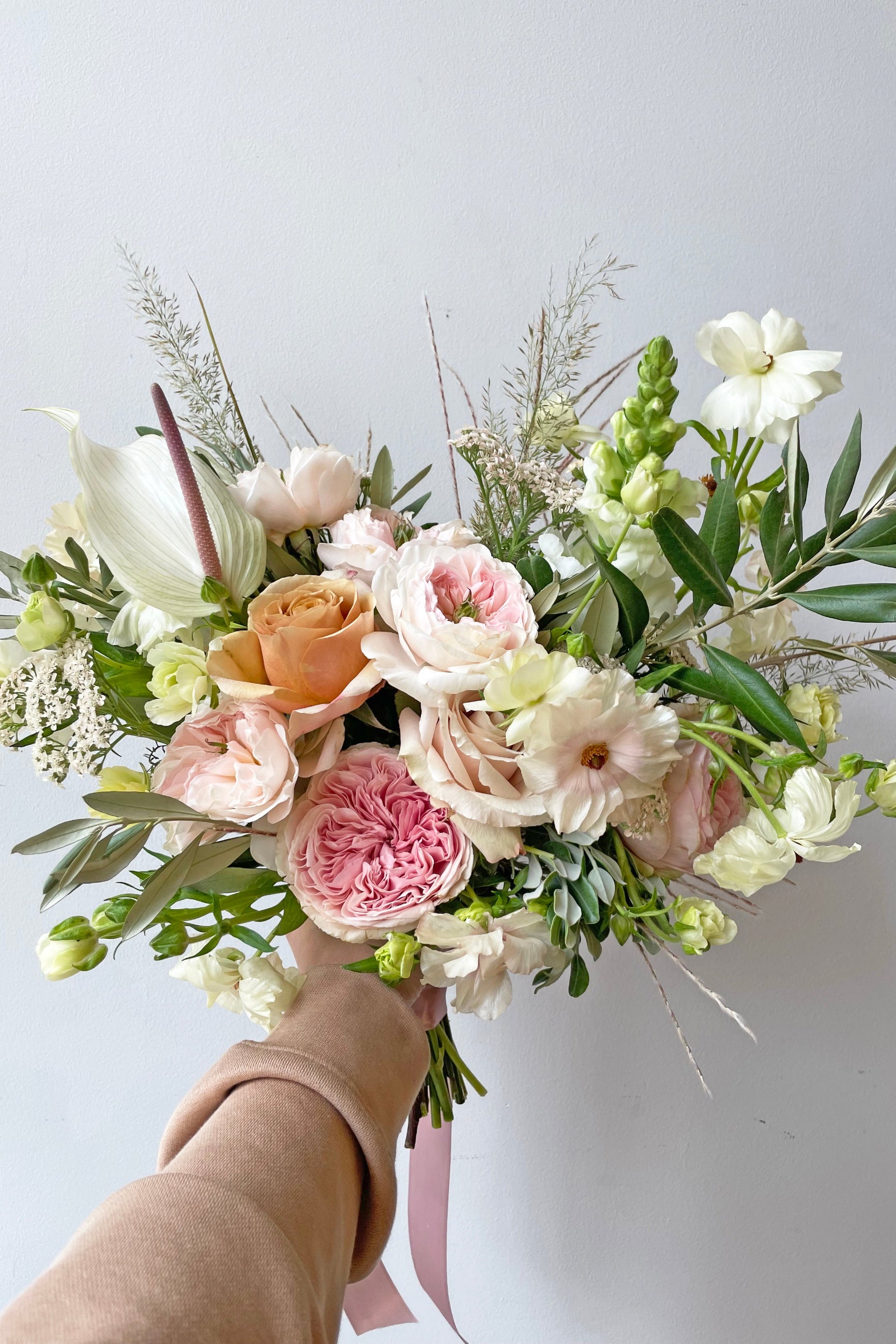 A hand holds an example a fresh Floral Arrangement Dawn with garden roses and white tufts from Sprout Home Floral ©Sprout Home #size_$200