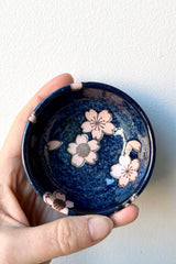 Namako pink sakura sauce dish shown from above against a white wall with a hand holding it to show scale. 