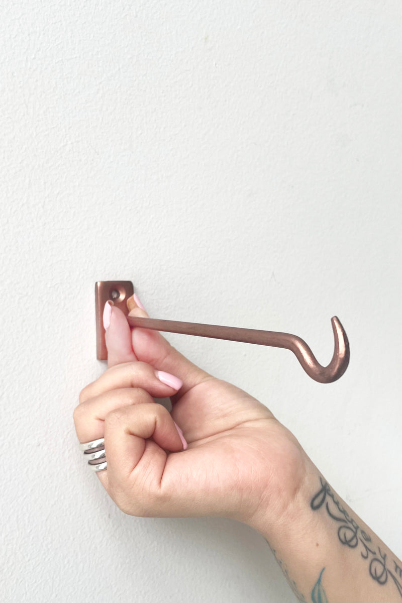 A hand holds Bijou Wall Hook copper against white wall