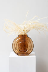 Retro Vase glass amber on white surface in a white room. Inside the vase are stems of bleached fern