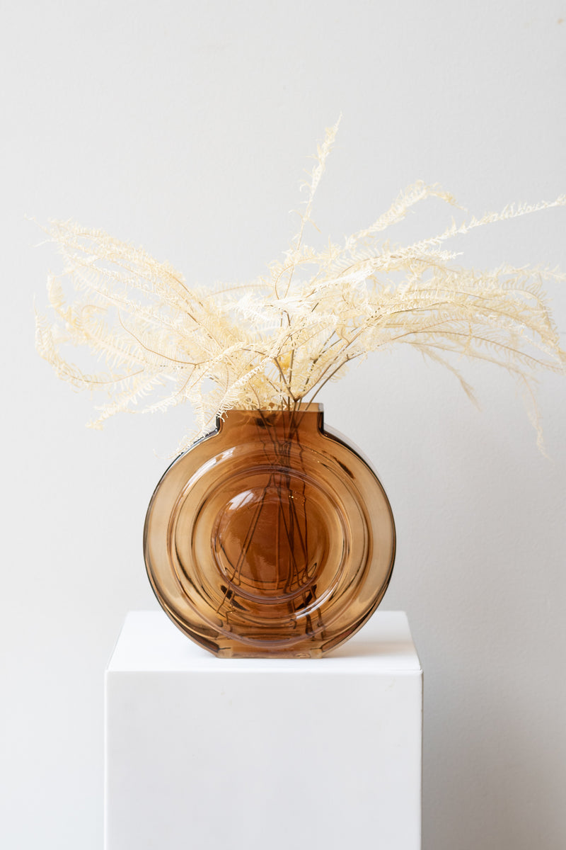 Retro Vase glass amber on white surface in a white room. Inside the vase are stems of bleached fern