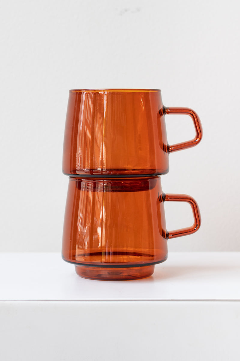 Two stacked Kinto sepia glass amber mugs on white surface in white room