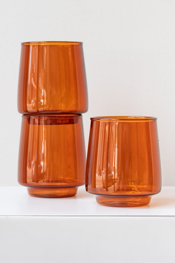 Three Kinto sepia glass amber tumblers on white surface in white room. Two are stacked and one is solo in front