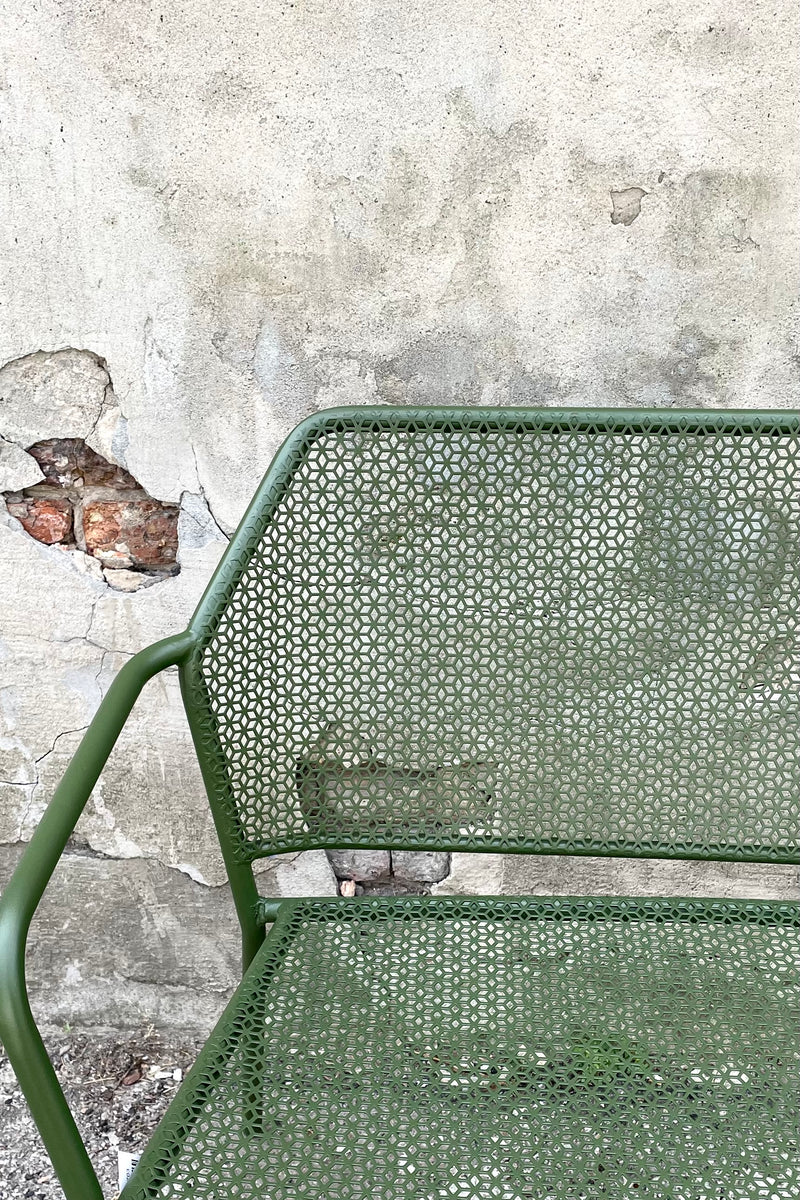 A close-up view of the Martini Iron Garden Bench in Moss against a concrete backdrop