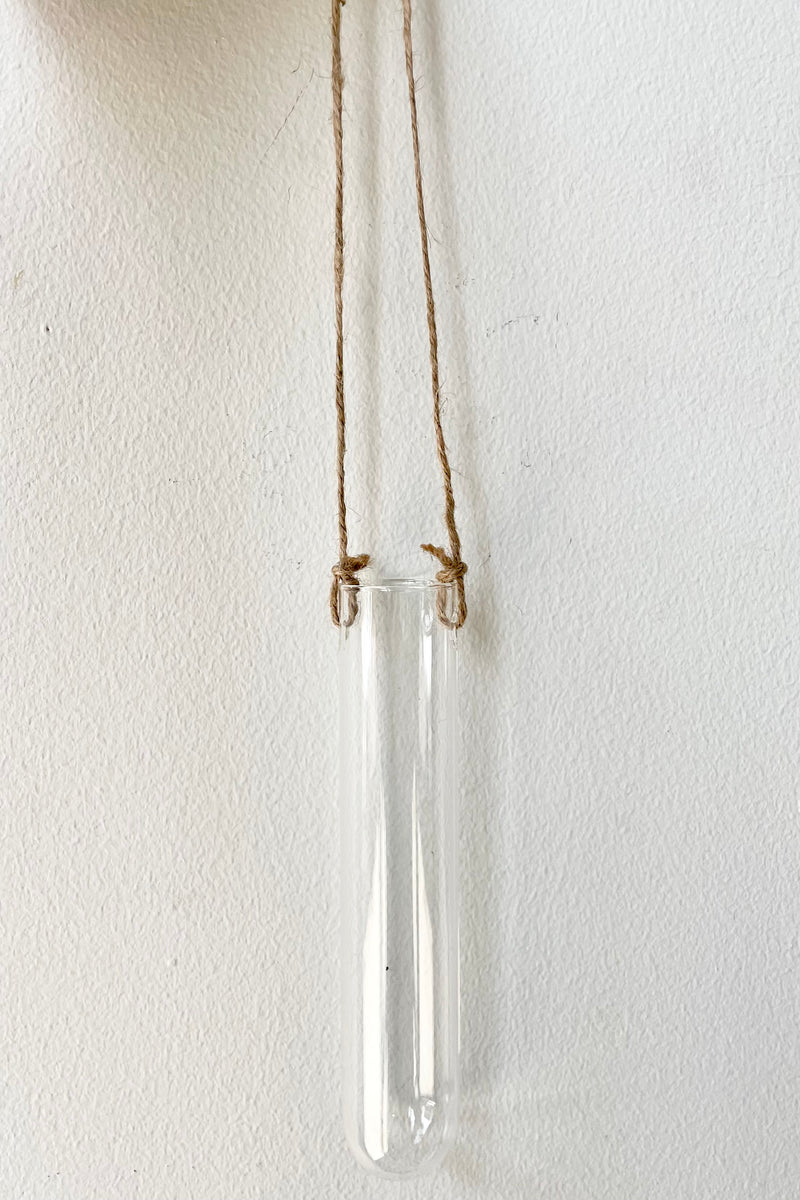 An empty small hanging glass vase against a white wall. 