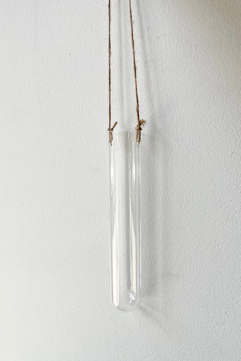 An empty hanging glass vase medium against a white wall. 