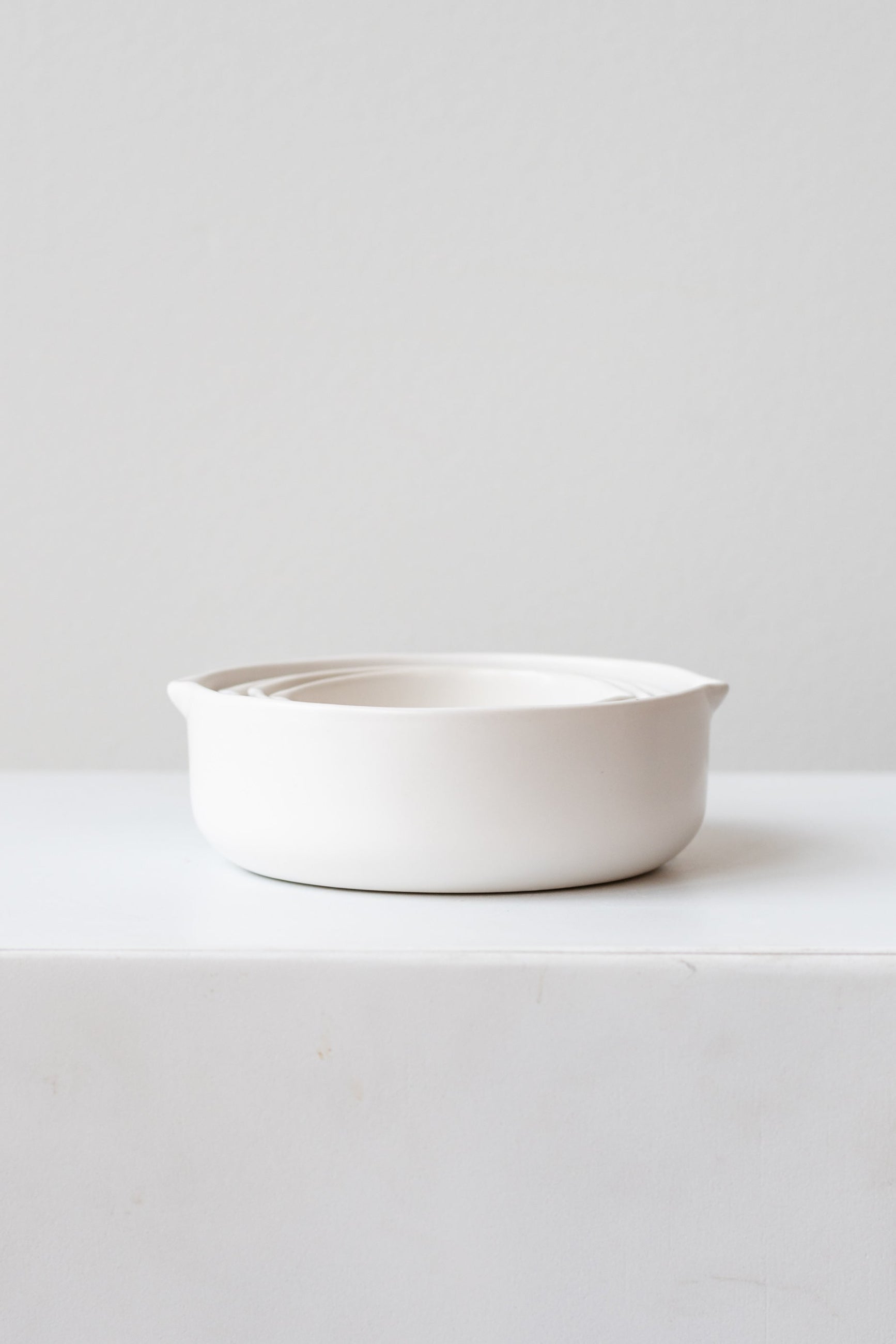 White circular Stoneware Measuring Cup Set nested on a white surface in a white room ©Sprout Home 