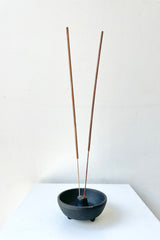 Incense Weight black with two insense sticks against a white wall  