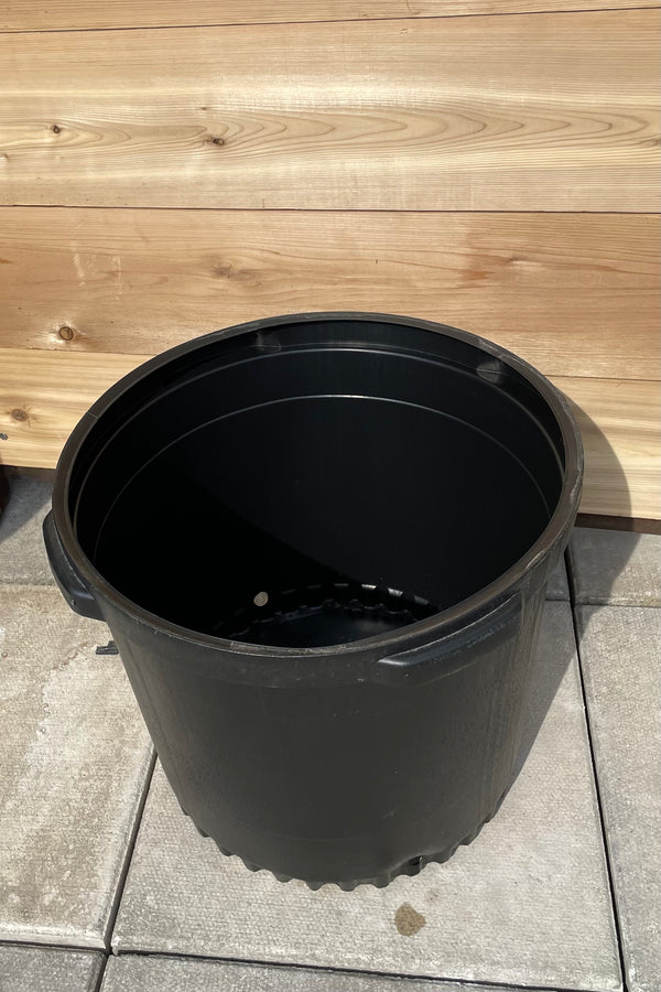 An 18" black growers pot shown against a cedar wall. 