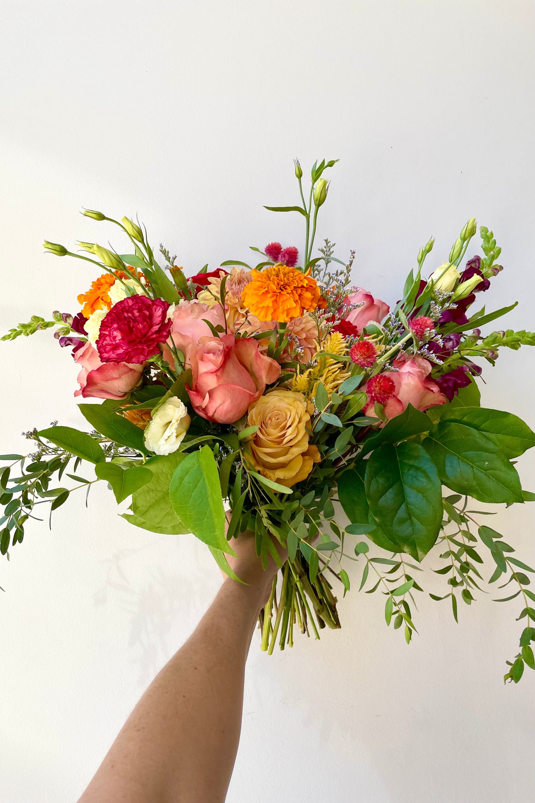 A hand holds a fresh floral arrangement by Sprout Home in the colorway Midday with golden roses and lisianthks against a white backdrop Sprout Home #size_$130