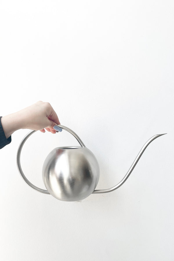 A hand holds Watering Can stainless steel from a side view against white backdrop