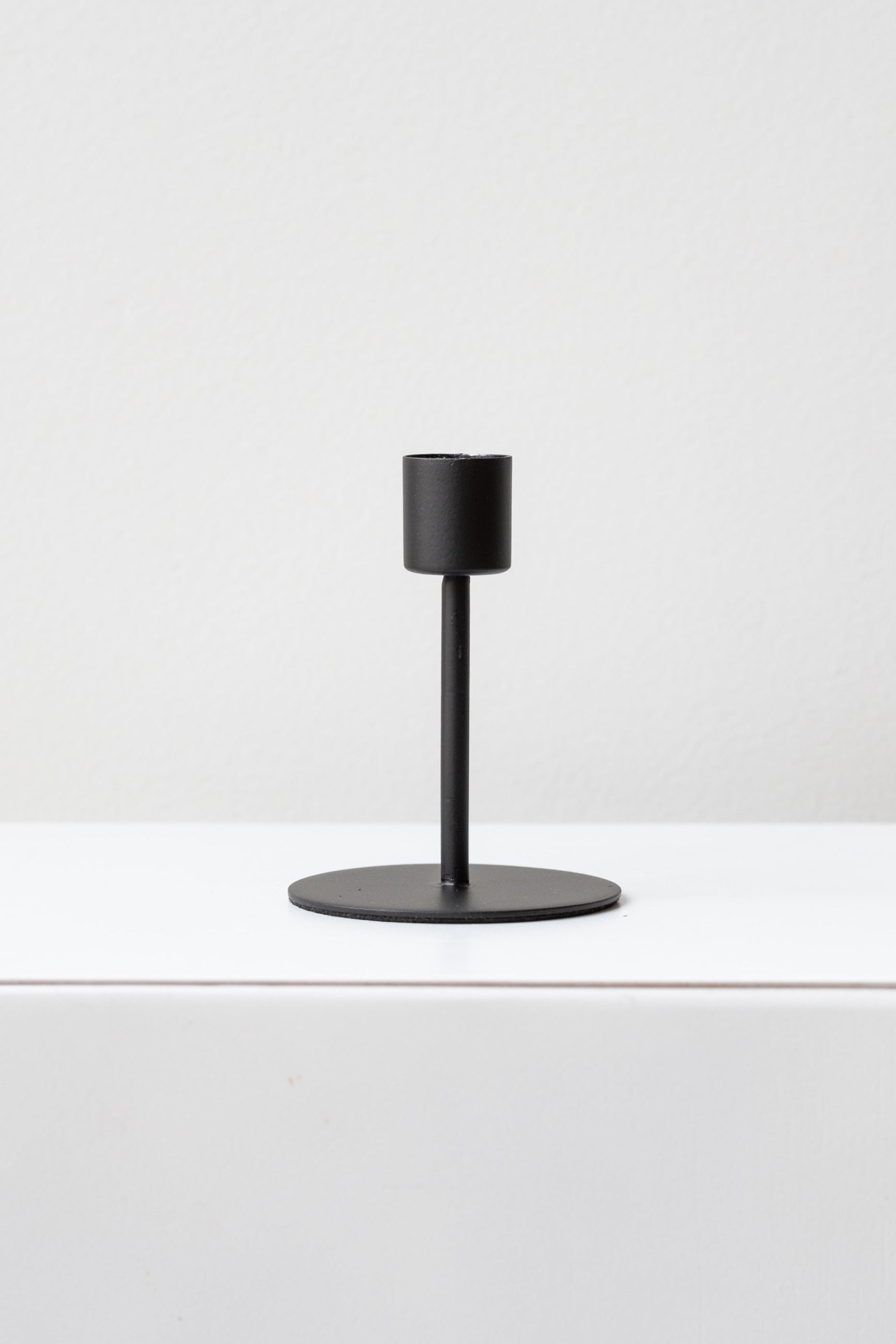 A sleek matte black taper candle holder with a minimalist design, holding a taper candle, on a white background. ©Sprout Home