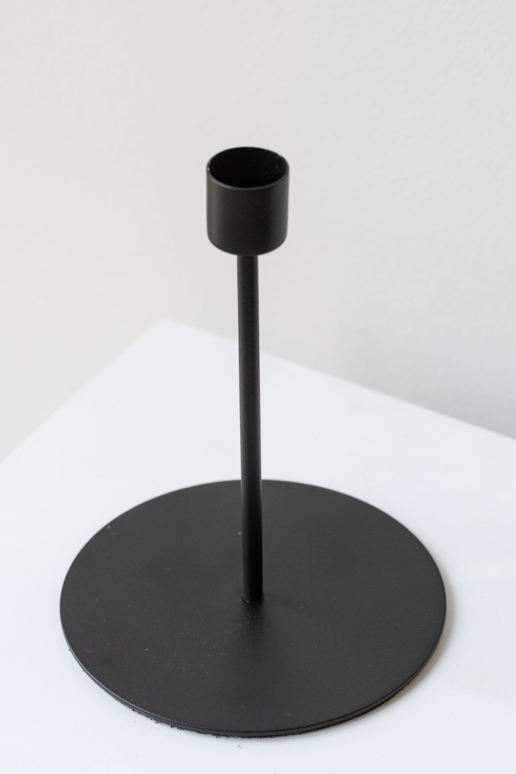 Black tall taper candle holder on a white surface in a white room ©Sprout Home