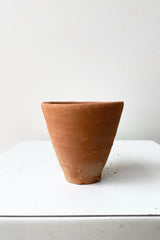 A picture of the simple terra cotta cup shown from the side against a white wall at Sprout Home.