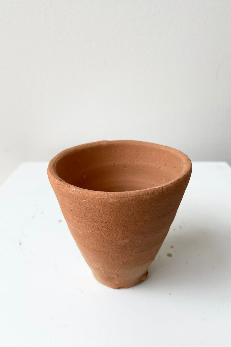 A picture of the simple terra cotta cup shown from the side and top against a white wall at Sprout Home.