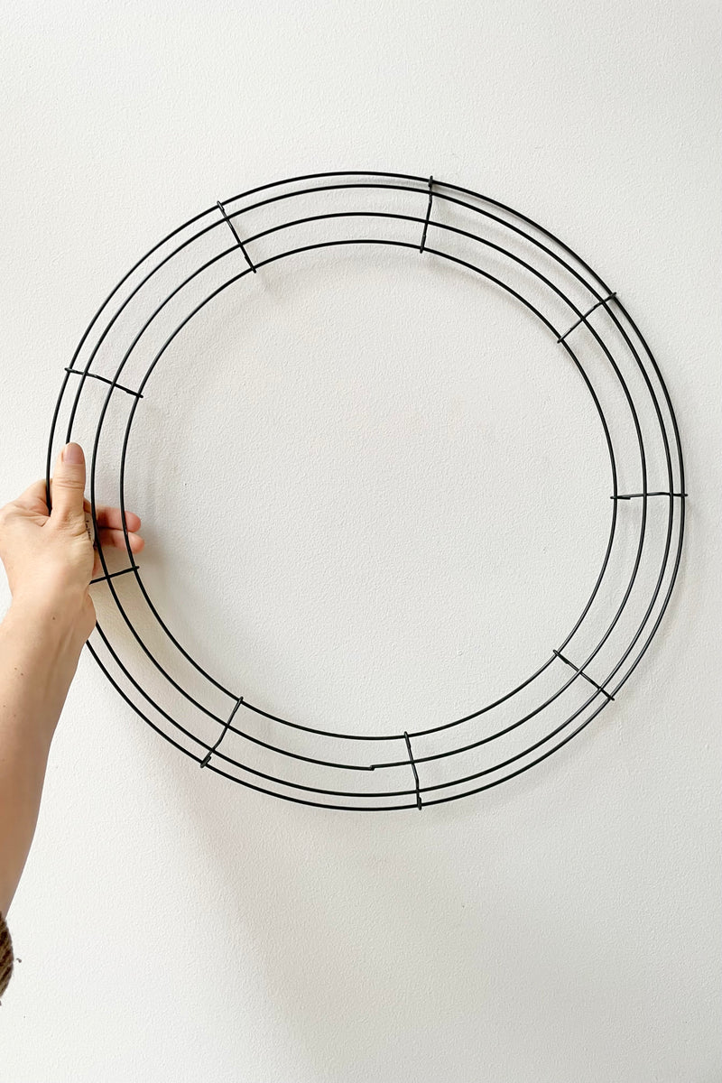 A hand holds the 18" wire wreath frame against a white backdrop. 