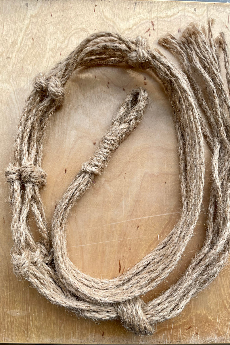 The natural jute macrame hanger rolled up on a birch piece of plywood. 