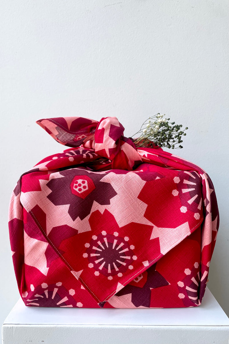 A frontal view of the 42" Square Furoshiki Pattern Flowers Red shown wrapped and knotted around a box
