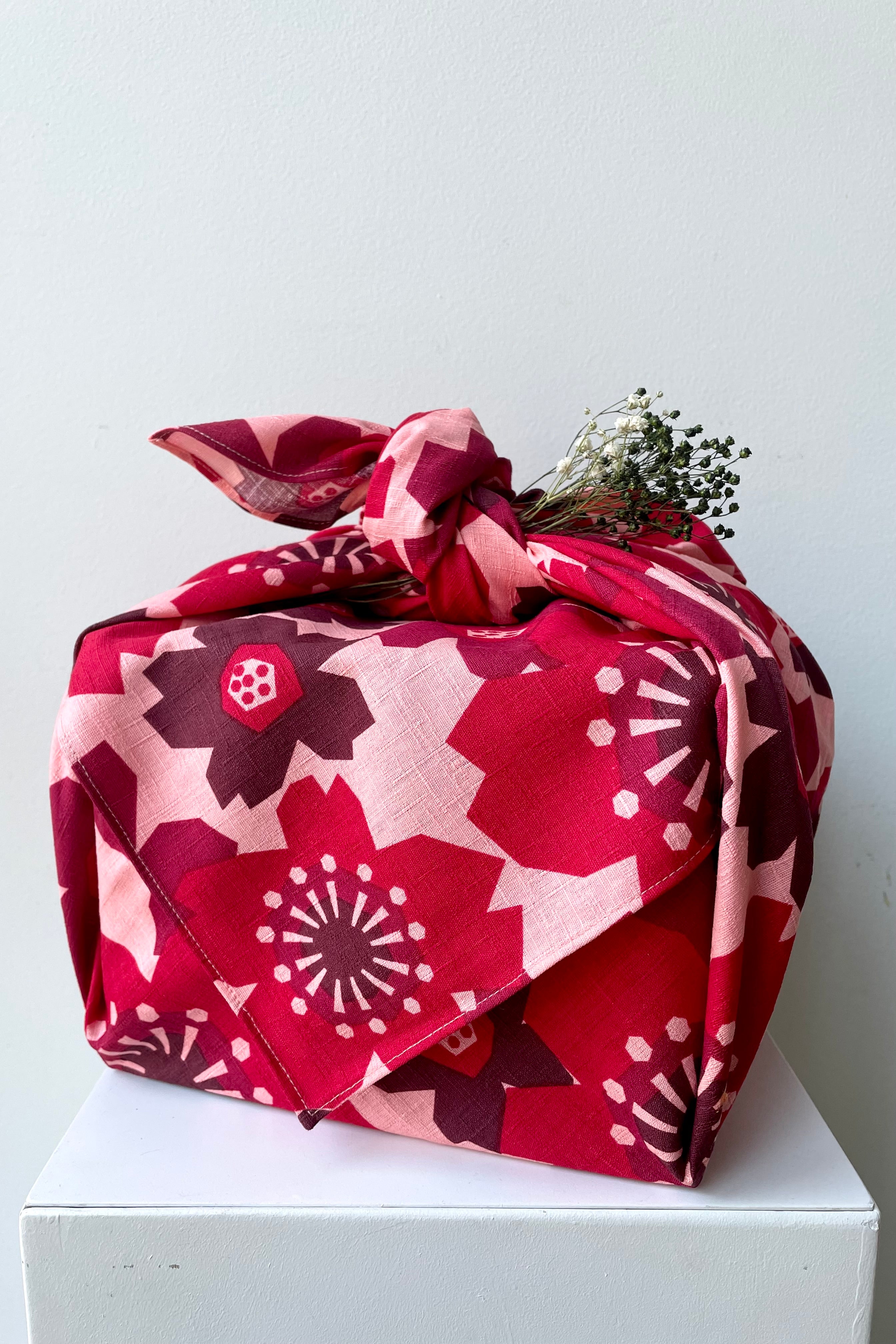 A frontal view of the 42" Square Furoshiki Pattern Flowers Red shown wrapped and knotted around a box