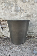 The 16" old bronze madison planter shown from the side against a concrete wall. 