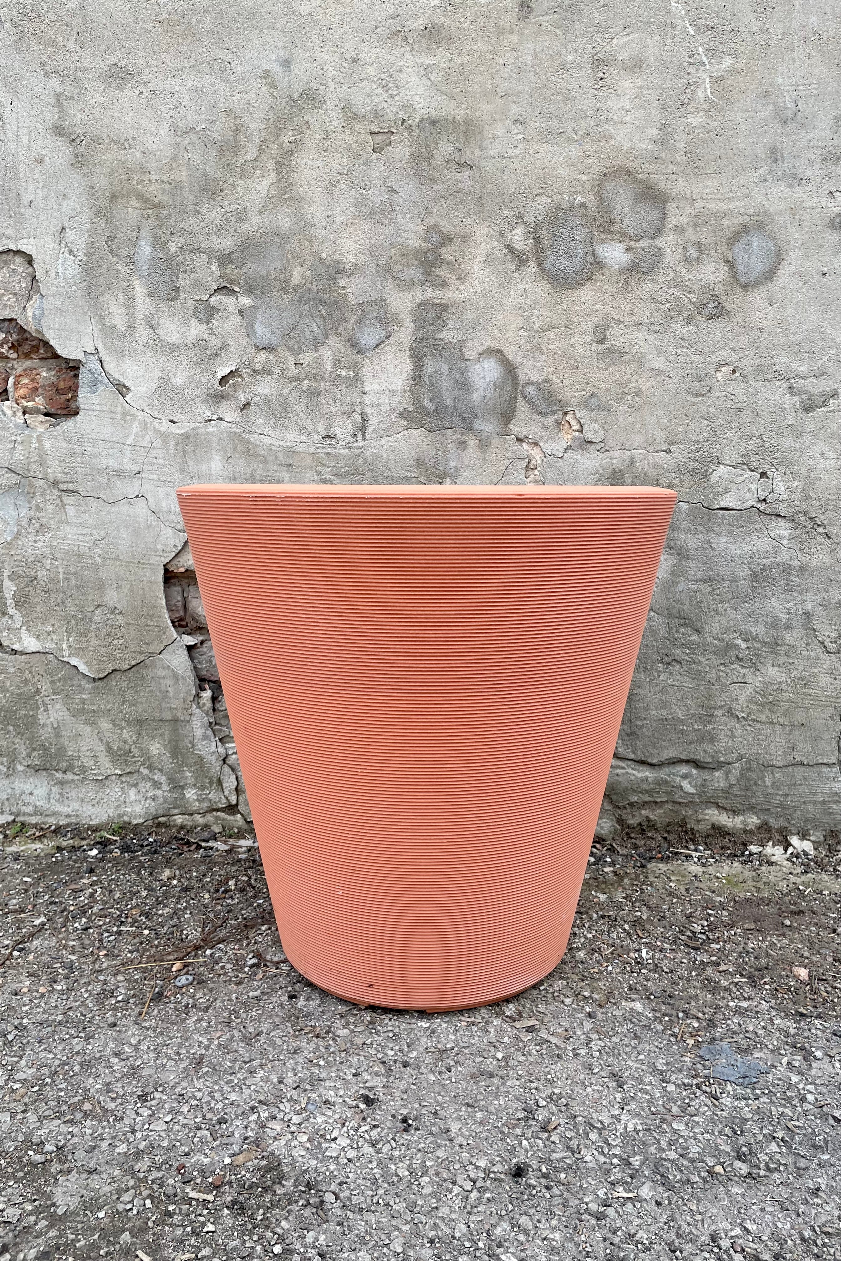 The weathered terracotta madison 20" container against a concrete wall. 