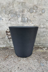 The outdoor Madison 20" planter in caviar black against a cement wall. 