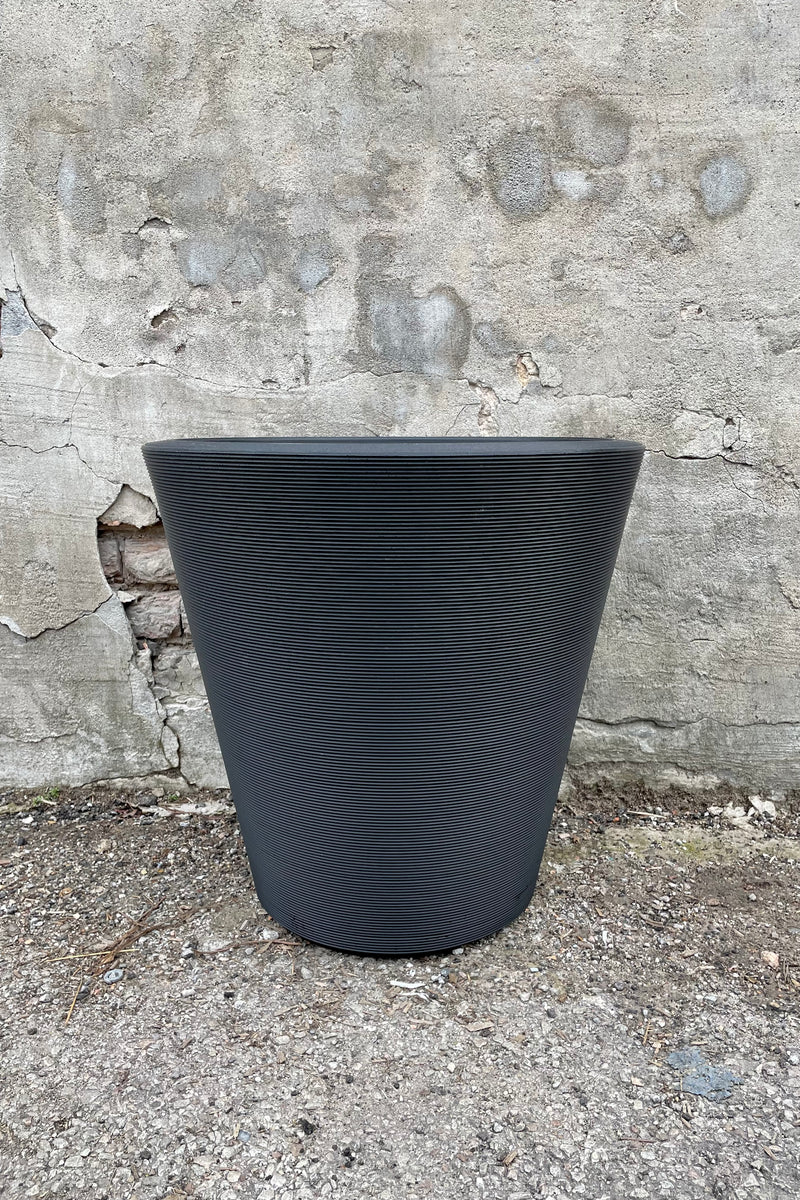 The outdoor Madison 20" planter in caviar black against a cement wall. 