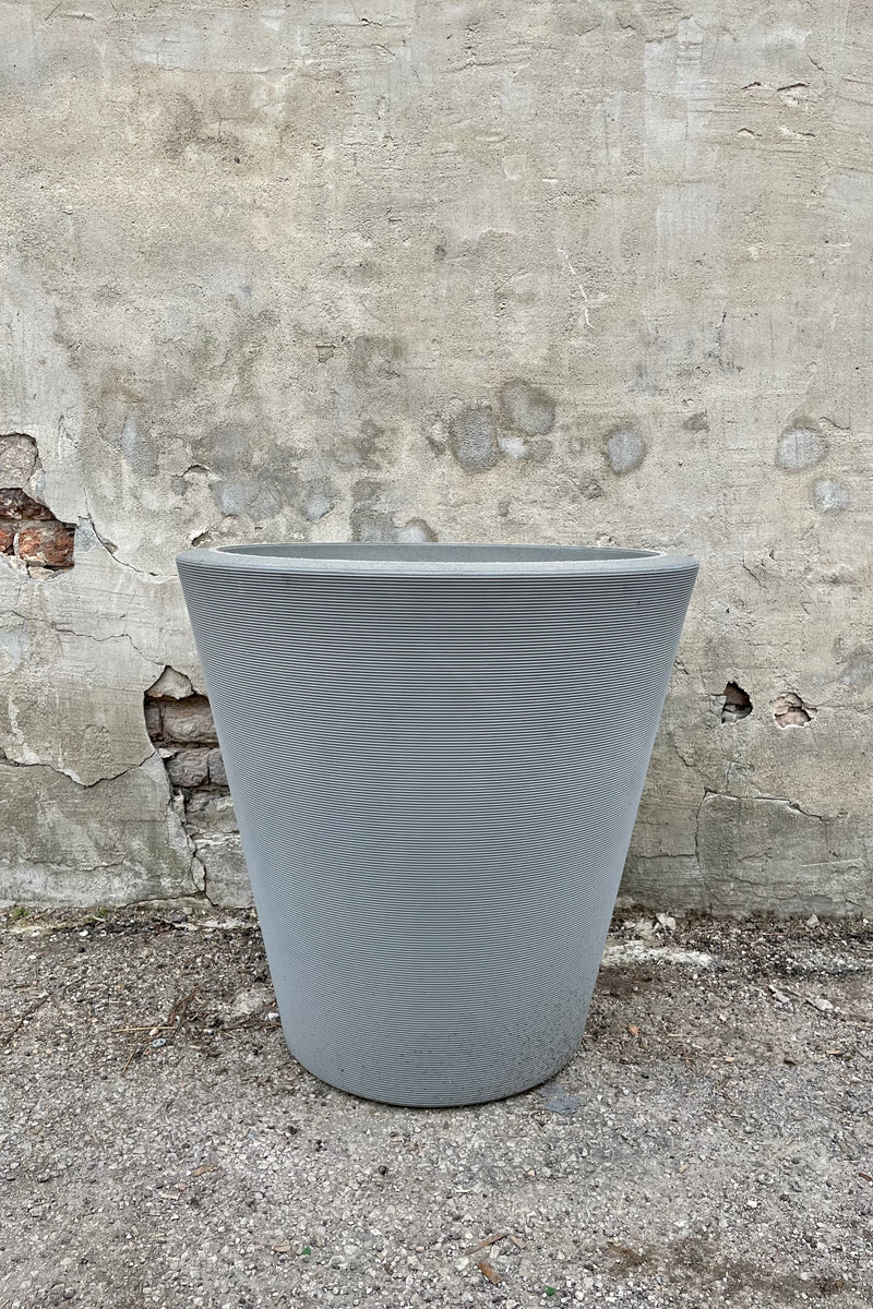 The Weathered grey Madison planter in a 26" diameter against a cement wall. 