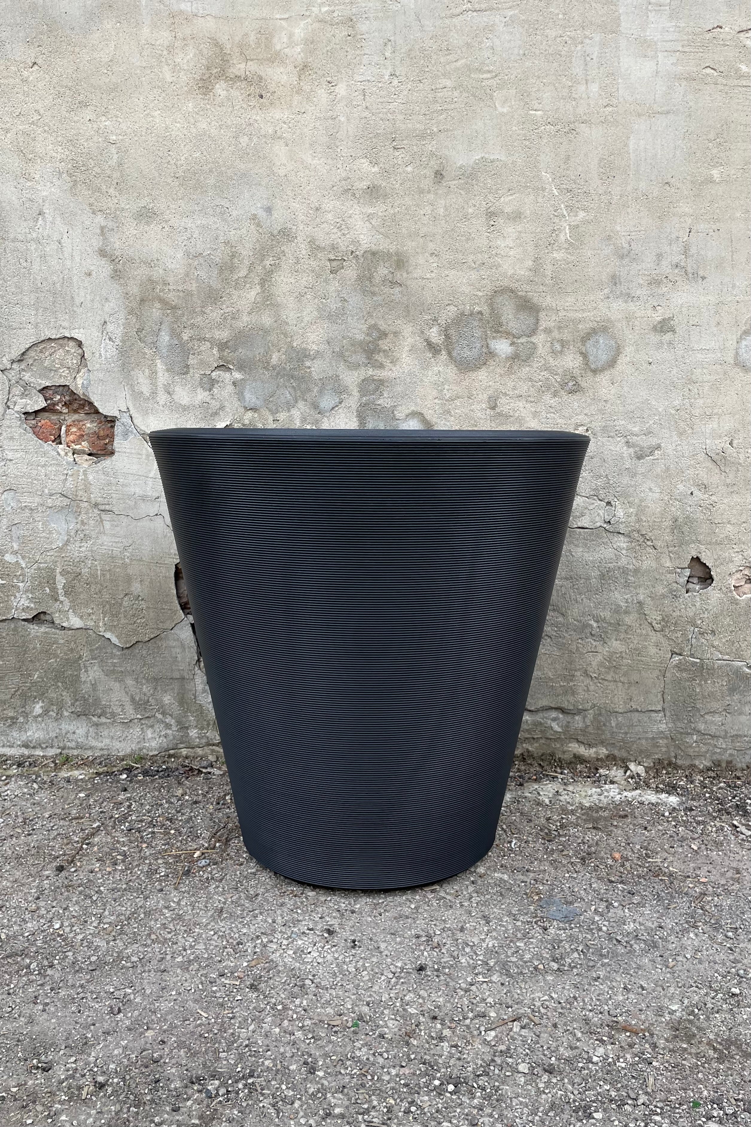 The Madison 26" container in Caviar Black against a concrete wall., 